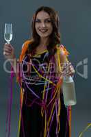 Smiling woman wrapped in multi color streamers holding champagne