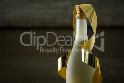 Champagne bottle with golden ribbon against wooden background