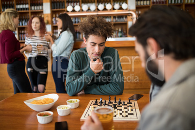 Two men playing chess while having glass of beer