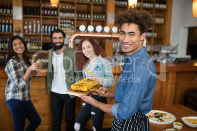 Smiling waiter serving tray of baby corn to customers