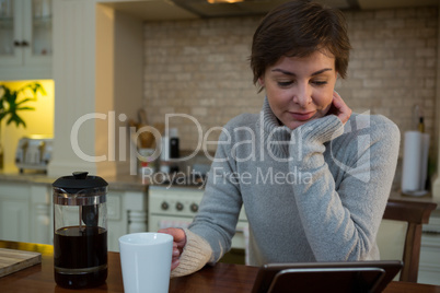 Woman using digital tablet while having cup of coffee in kitchen
