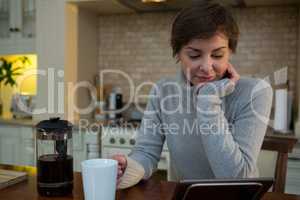 Woman using digital tablet while having cup of coffee in kitchen