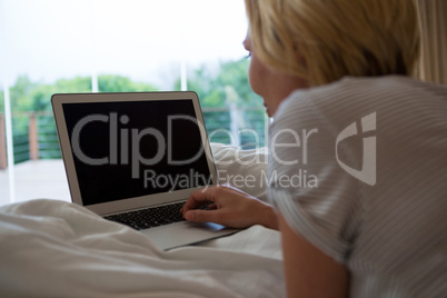 Woman using laptop while relaxing on bed