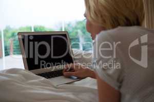 Woman using laptop while relaxing on bed