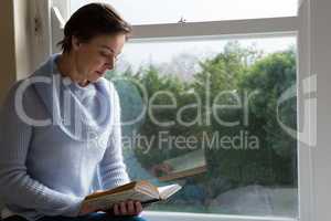 Woman reading book on windowsill