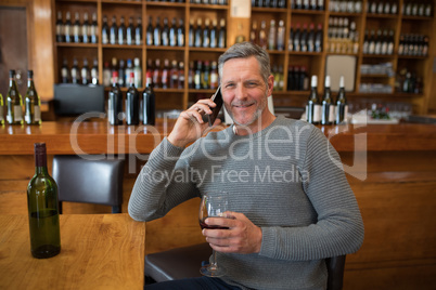 Smiling senior man talking on mobile phone while having red wine