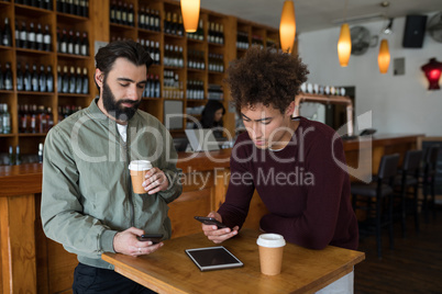 Two male friends using mobile phone while having coffee