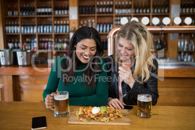Two female friends having glass of beer and mexican food in bar