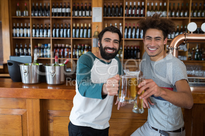 Two friends toasting glass of beer at counter in bar
