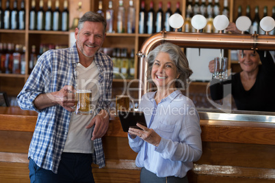 Friends using digital tablet while having glass of beer at counter