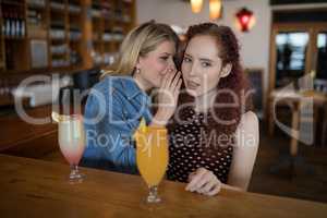 Woman whispering in her friends ears at counter