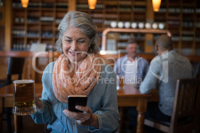 Smiling senior woman using mobile phone while having glass of beer