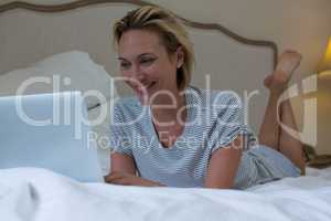 Woman using laptop while relaxing on bed