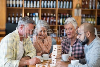 Happy friends playing jenga game while having cup of coffee