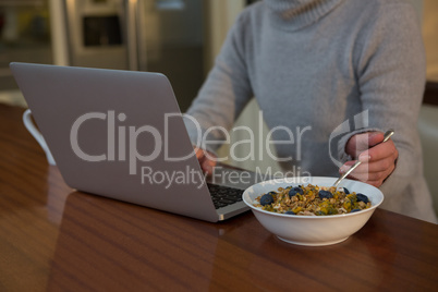 Mid section of woman having breakfast while using laptop
