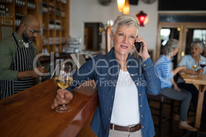 Senior woman talking on mobile phone while having glass of wine