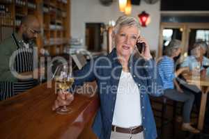 Senior woman talking on mobile phone while having glass of wine