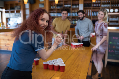 Woman playing beer pong game with friends in bar