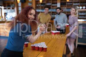 Woman playing beer pong game with friends in bar