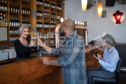 Senior waitress serving glass of beer to customer at counter