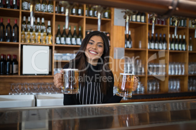 Smiling waitress holding glass of beer at counter