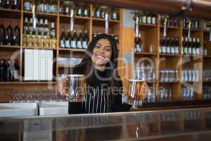 Smiling waitress holding glass of beer at counter