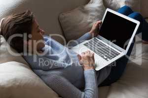 Woman using laptop while relaxing on sofa