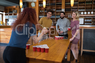 Friends playing beer pong on table in bar