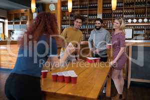 Friends playing beer pong on table in bar