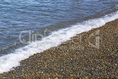Surf wave on the beach with sea pebbles.
