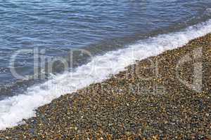 Surf wave on the beach with sea pebbles.