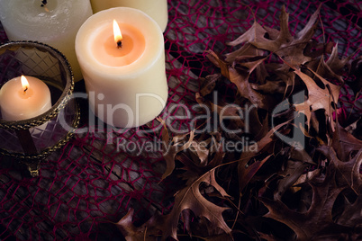Lit candles and dry leaves on table