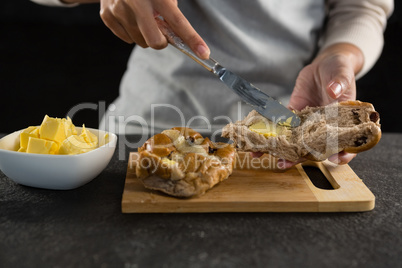 Woman applying butter over multigrain bun slice