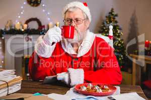 Santa Claus having coffee while holding a letter