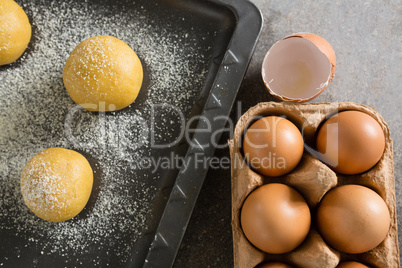 Egg carton and dough balls with icing sugar on baking tray