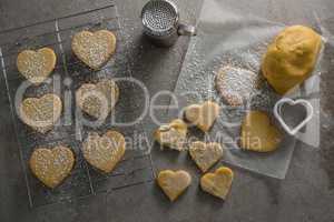 Raw heart shape cookies on baking tray with flour shaker strainer, cookie cutter and wax paper