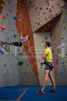 Man holding rope looking at athlete climbing wall in fitness club