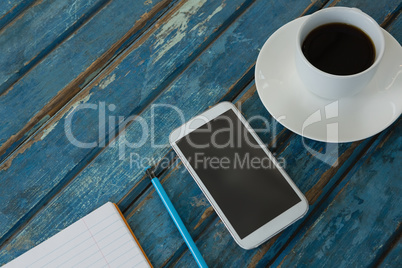 Black coffee, mobile phone, pencil and book on wooden plank