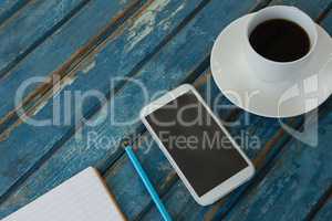 Black coffee, mobile phone, pencil and book on wooden plank