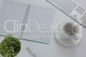 Keyboard, pot plant, pen, book, coffee cup and saucer on table