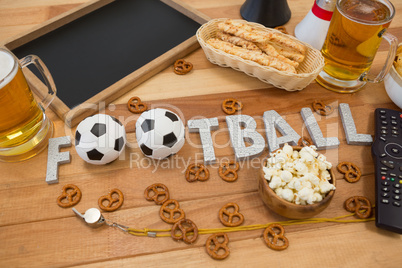 Remote control, slate, snacks, drinks and football word arranged on table