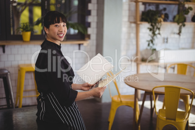 Portrait of young waitress holding menu while leaning on table