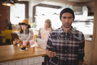 Portrait of young man holding eyeglasses standing against female friends