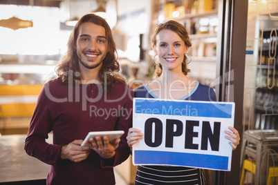 Portrait of smiling waitress holding placard while standing by man with digital tablet