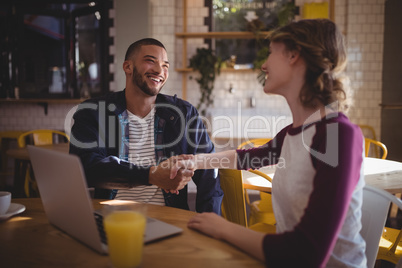 Smiling young friends shaking hands while sitting with laptop