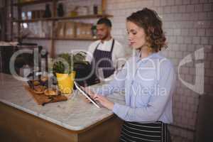 Young waitress using tablet computer while standing at counter