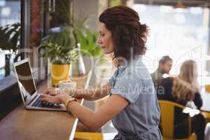 Side view of woman using laptop at counter in cafe