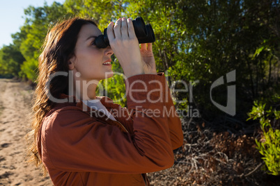 Woman looking through binocular by tree