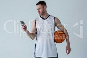 Player holding basketball while using mobile phone