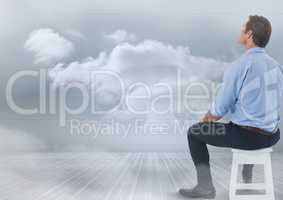 Businessman sitting on stool with clouds in room